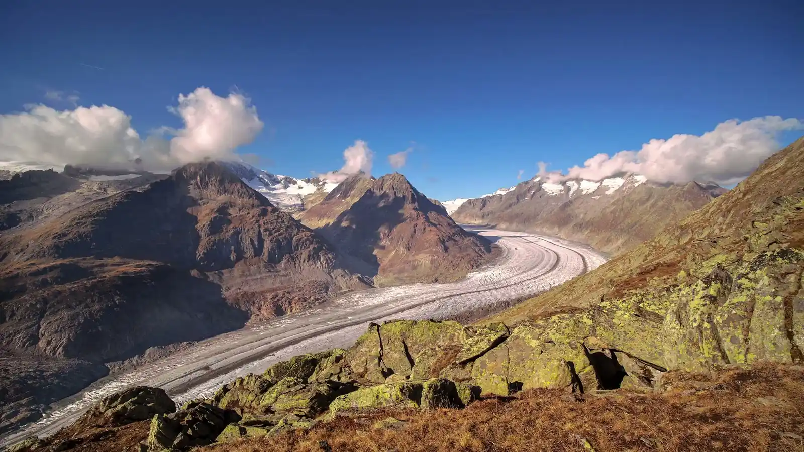 Schweizer Alpenpanorama im Morgenlicht mit Wanderweg und rot-weissem Wegmarkierungspfosten